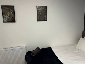A hotel room with a bed, a radiator, and two framed wall art pieces.