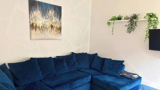 Una sala moderna con un sofá seccional azul, una mesa de centro de vidrio y un televisor montado.