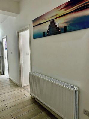 A hallway with a white radiator, a door, and a wall-mounted painting of a sunset over a pyramid.
