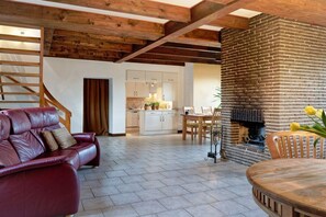 A living room with a red leather sofa, a wooden dining table, and a brick fireplace. - Holiday home with 3 bedrooms (Groß Zecher)