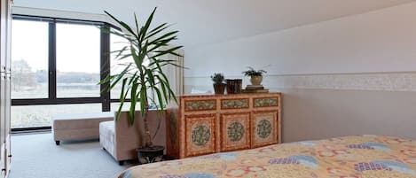 Un dormitorio con una cama grande, un aparador, una planta en maceta y vistas al exterior a través de una ventana.