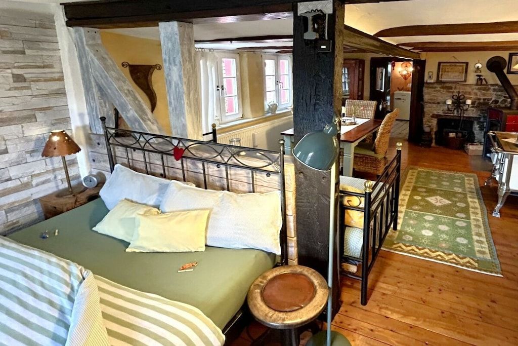 A room with a bed, a wooden floor, a stone wall, and a window.