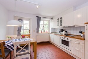 Eine Küche mit weißen Schränken, einer Holz Arbeitsplatte, einem Herd und einem Fenster mit Vorhängen.