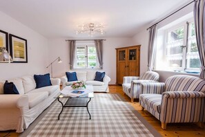 A living room with a white sofa, striped armchairs, a coffee table, and a wooden cabinet. - Holiday apartment with 2 bedrooms (Krummhörn-Greetsiel)