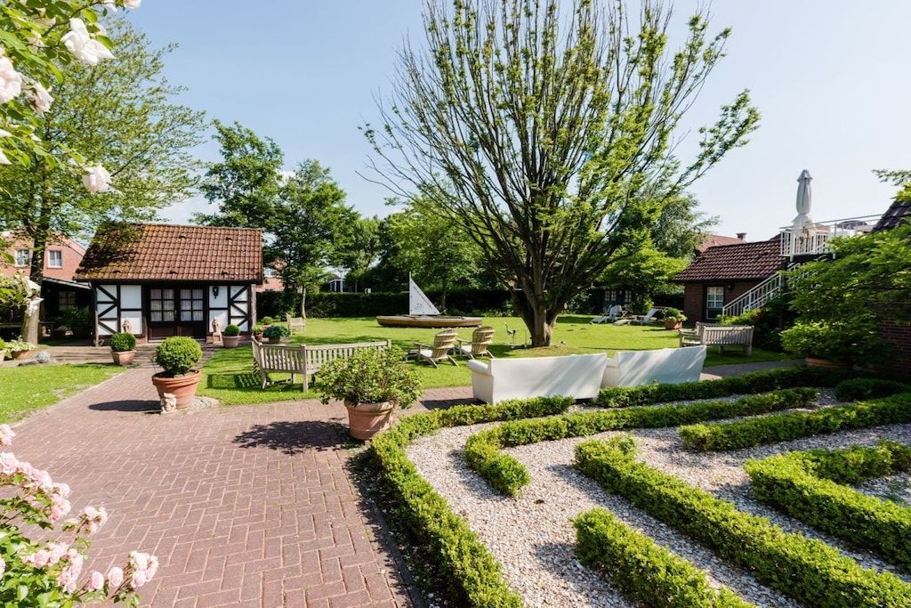 A garden with a paved walkway, neatly trimmed hedges, and a variety of potted plants.