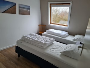 Ein Schlafzimmer mit zwei Betten, einem Fenster, einem Sessel und Wandbildern.
