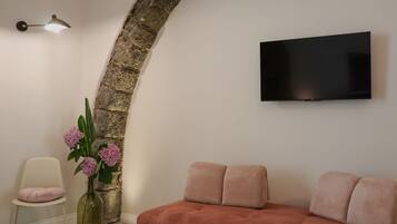 Un soggiorno moderno con un arco in pietra, un televisore a schermo piatto montato a parete, un divano rosa, una poltrona bianca e un vaso con fiori.