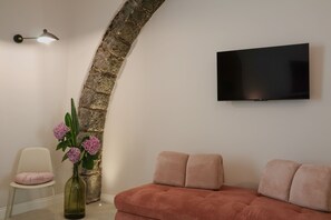 Una sala de estar moderna con un arco de piedra, un televisor de pantalla plana montado en la pared, un sofá rosa, una silla blanca y un jarrón con flores.
