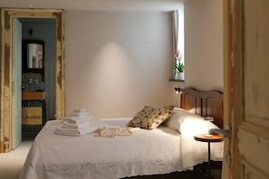 A bedroom with a bed, a bedside table, a nightstand, a window with a plant, and a door leading to another room. - LA BARONESSA (Riposto)