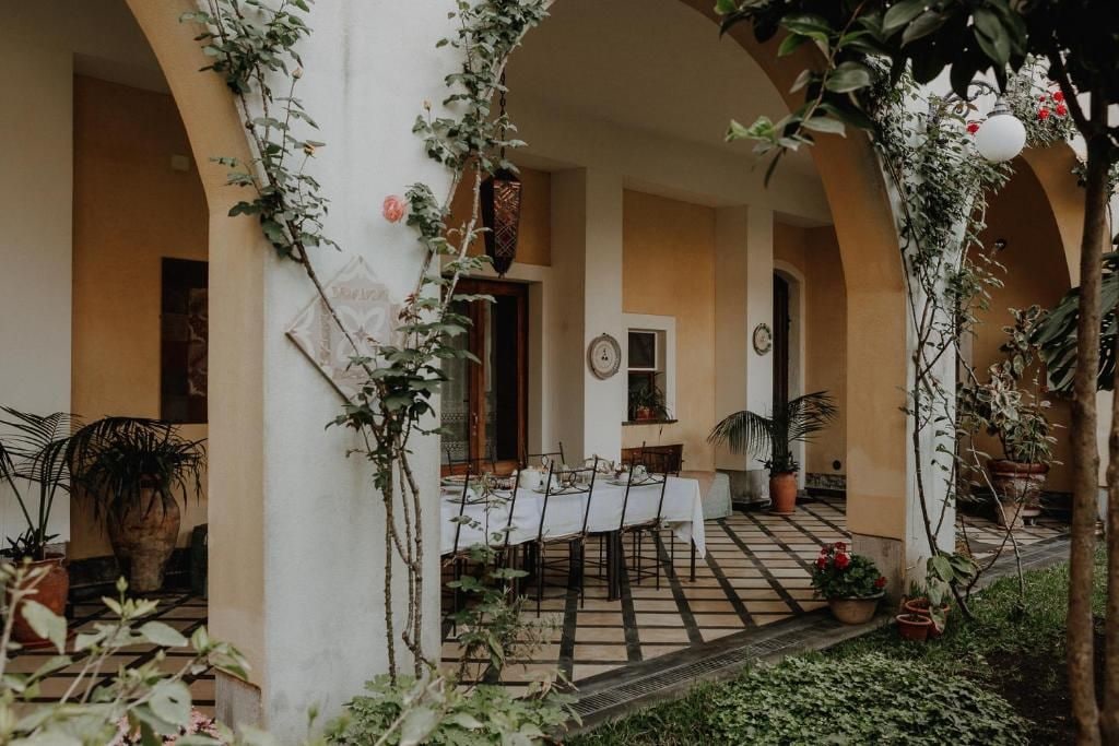 Un área de comedor al aire libre con una mesa para dos, rodeada de plantas en macetas y un piso de baldosas.