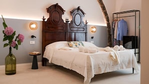 Un dormitorio con una cama de madera, una mesita de noche pequeña, un jarrón con flores y un perchero.