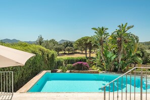 Une piscine offrant une vue sur un jardin aménagé et sur des montagnes lointaines.
