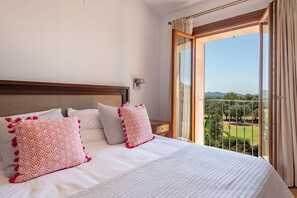 A hotel room with a large bed, a nightstand, a wall-mounted lamp, and a balcony with a view of the landscape. - Can Porquer, Luxury villa with a pool near the golf course (IB Pollensa)