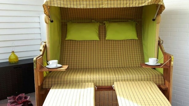 Ein Zimmer mit einem Schlafsofa mit Schachmuster, zwei grünen Kissen, einem kleinen Tisch mit Tasse und Untertasse sowie einer Korbschaukel.