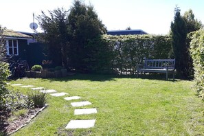 A backyard with a grassy lawn, a stone pathway, a bench, and a hedge. - Holiday home with 2 bedrooms (Butjadingen)