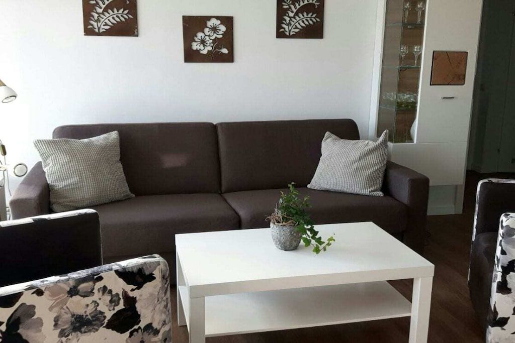 Een woonkamer met een bruine bank, een witte salontafel en fauteuils met een patroon.