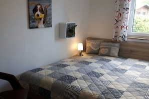 A bedroom with a bed, a nightstand, a wall-mounted plant, and a window with curtains. - Holiday home with 2 bedrooms (Butjadingen)