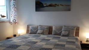 Ein Schlafzimmer mit Bett, Nachttisch, Lampe, einem Bild an der Wand und einem Fenster mit Vorhängen.