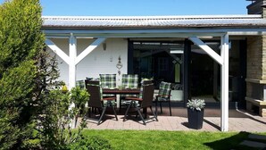 Eine überdachte Terrasse mit Tisch, Stühlen, einem Blumentopf und Blick ins Haus.