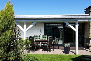 Une terrasse couverte avec une table et des chaises, une plante en pot et une vue sur l’intérieur de la maison.