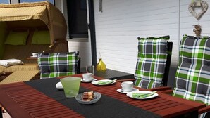 Eine Terrasse mit Tisch für zwei Personen, Korbmöbeln und einer Zierwand.