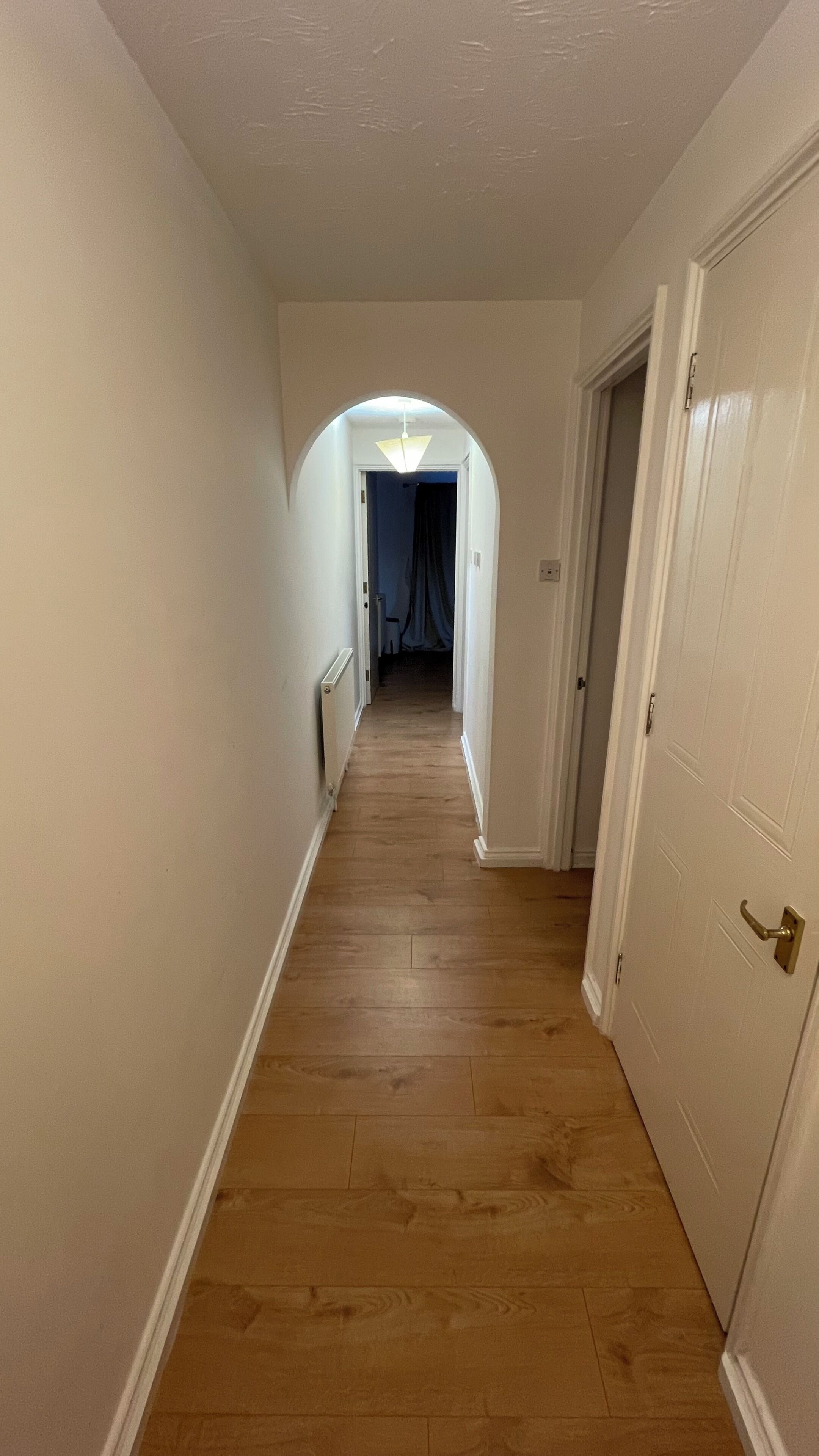 A hallway with wooden flooring, white walls, and a door on the right.