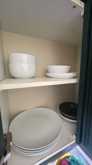 A kitchen shelf with stacked white plates and bowls.