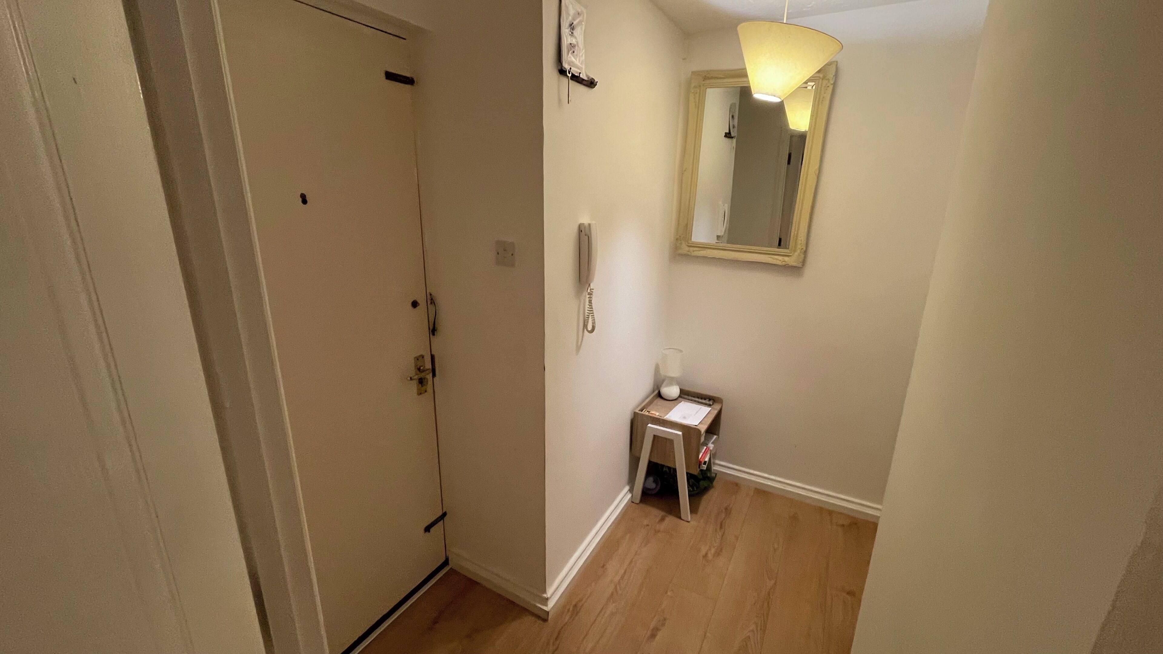 A hallway with a door, a small table with a lamp, and a mirror on the wall.