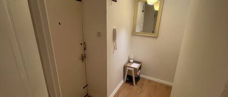 A hallway with a door, a small table with a lamp, and a mirror on the wall.
