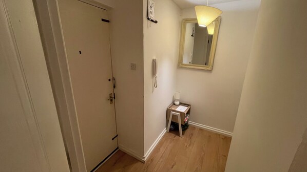 A hallway with a door, a small table with a lamp, and a mirror on the wall.