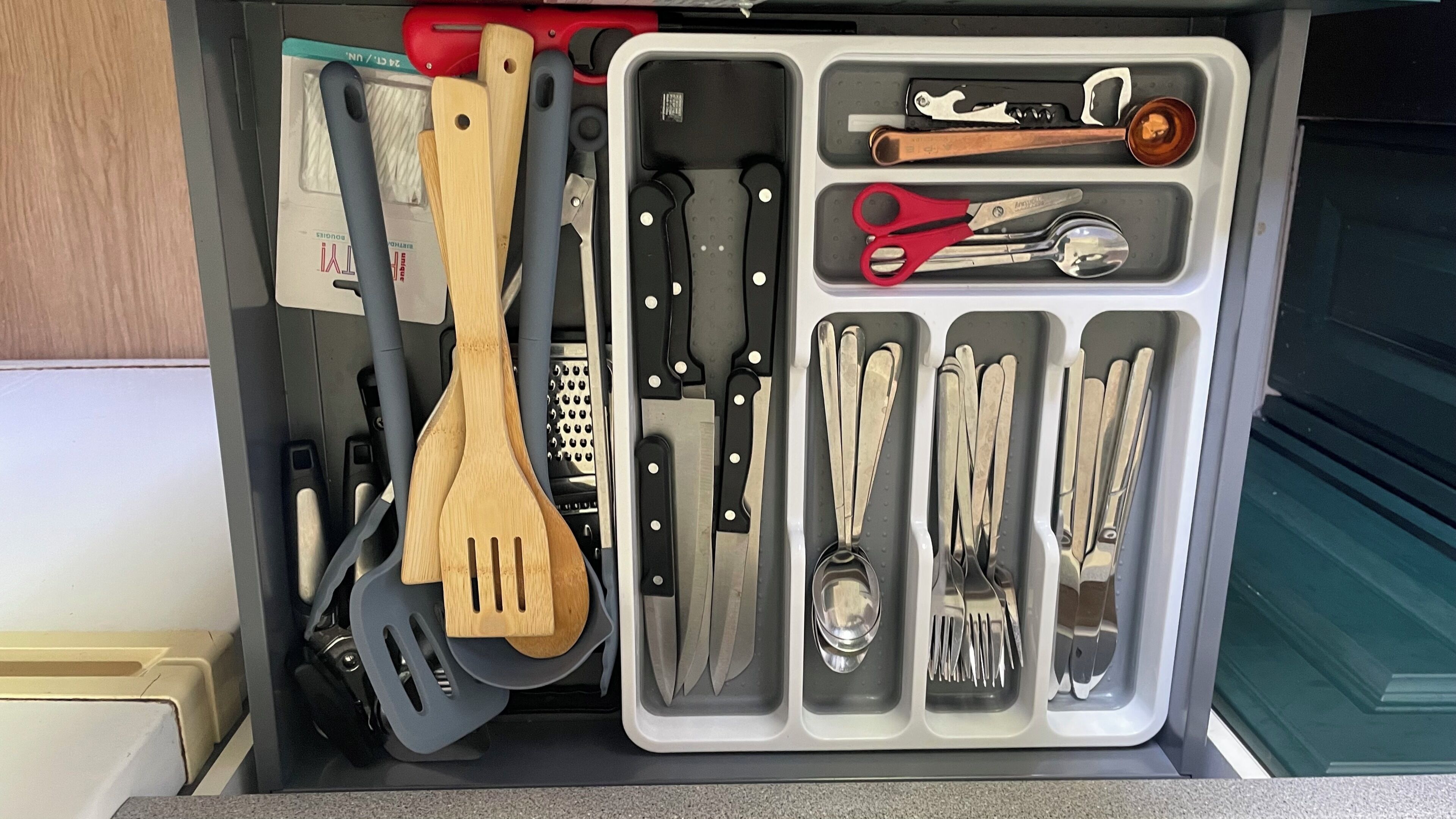 A drawer with various kitchen utensils organized in compartments.