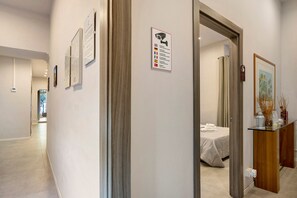 A hotel corridor with framed informational posters, a security warning sign, and a glimpse of a bedroom with a bed and a nightstand. - Deluxe Room with Balcony, Wi-Fi & Air Conditioning (Napoli)
