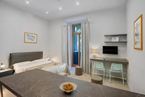 A modern hotel room with a bed, a desk, a TV, and a view of the outdoors. - Deluxe Room with Balcony, Wi-Fi & Air Conditioning (Napoli)