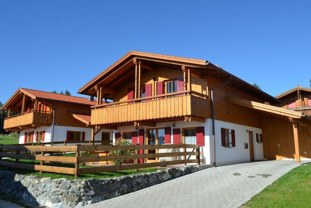 A chalet-style building with a wooden facade, multiple balconies, and a stone wall in front.