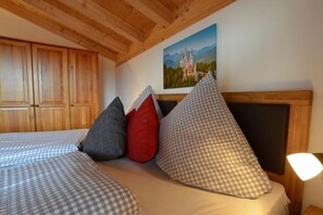A bedroom with a wooden ceiling, a bed with checkered bedding, a painting of a castle, and a nightstand with a lamp. - Holiday home in Allgäu with 3 bedrooms (Lechbruck am See)