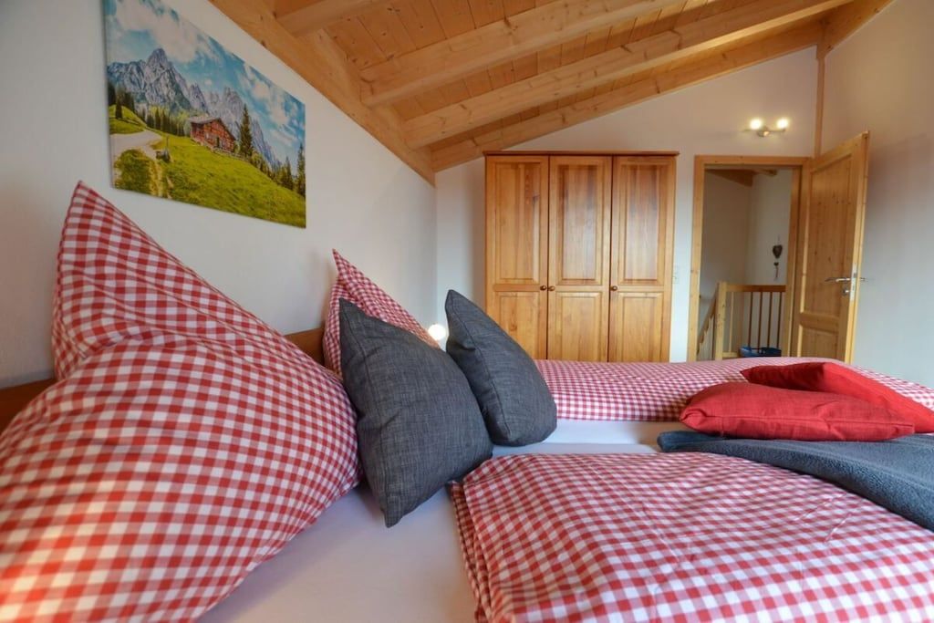 Una habitación con cama, ropa de cama a cuadros, un cuadro, armarios de madera y una puerta.