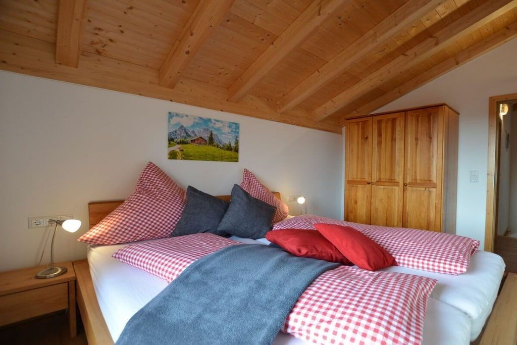 Ein Schlafzimmer mit Holzboden, einem Bett mit karierter Bettwäsche, einem Nachttisch, einem Kleiderschrank und einem Bild an der Wand.