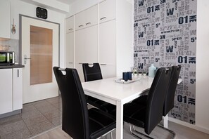Een moderne eetruimte met een witte tafel, zwarte stoelen en een muur met een herhalend patroon.