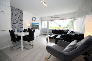 A modern living room with a grey sofa, a dining table with chairs, and a large flat-screen TV. - Meerliebe by Flo & Kim: Your modern apartment just 300 meters from the North Sea beach (Büsum)