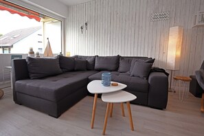 A modern living room with a dark grey sectional sofa, a small white side table, and a wooden floor. - Meerliebe by Flo & Kim: Your modern apartment just 300 meters from the North Sea beach (Büsum)