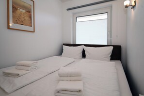 A neatly made bed with white linens and pillows, a window with blinds, and a framed picture on the wall. - Meerliebe by Flo & Kim: Your modern apartment just 300 meters from the North Sea beach (Büsum)