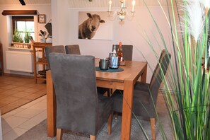 Ein Essbereich mit einem Holztisch, grau gepolsterten Stühlen, einer Kronleuchter und einem Wandbild von einem Schaf.