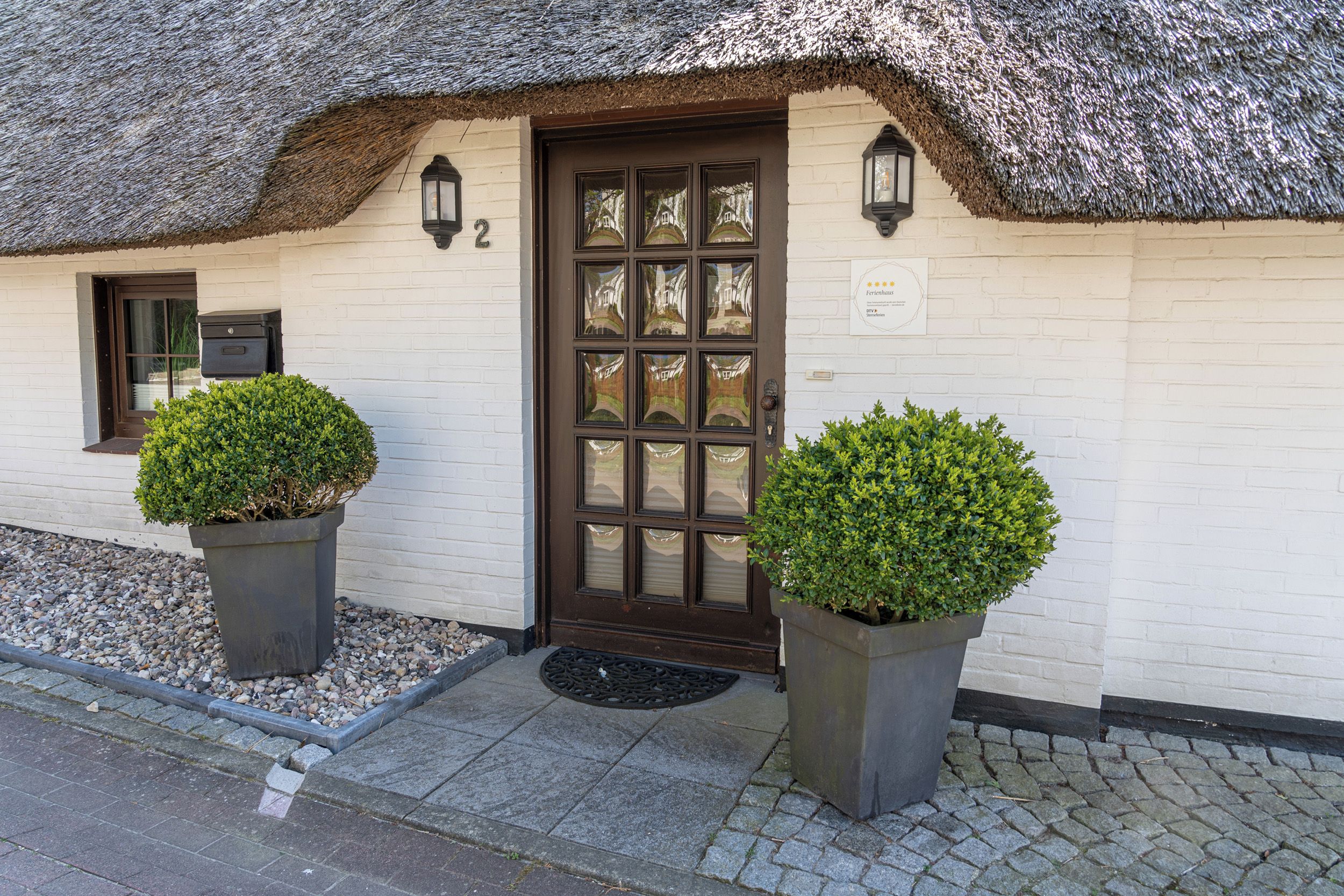 A traditional building with a thatched roof, a wooden door with glass panels, and two potted plants on the ground.