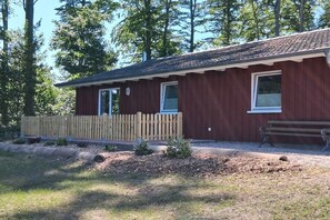 Un bâtiment en bois d’un seul étage, doté d’un porche, d’une clôture en bois et d’un banc.