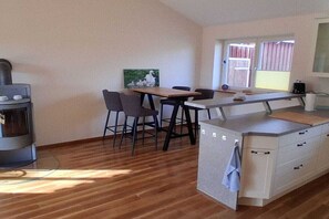 A compact kitchen with a central island, bar stools, a stove, and a window with a view. - Holiday home De lütte Ruhestuuv (Waabs)