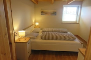A small, cozy bedroom with a single bed, a nightstand with a lamp, and a window providing natural light. - Holiday home De lütte Ruhestuuv (Waabs)