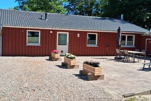 Un bâtiment rouge avec un toit en tuiles, une terrasse en gravier et du mobilier d’extérieur.