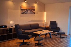 A modern living room with a sofa, two armchairs, a coffee table, and a painting on the wall. - Holiday home De lütte Ruhestuuv (Waabs)