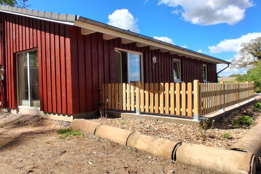 Un edificio rojo con una terraza de madera y una valla de metal.