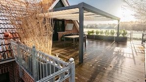 Un espace extérieur abrité doté d’une terrasse en bois, d’un bâtiment en briques et offrant une vue sur une étendue d’eau.